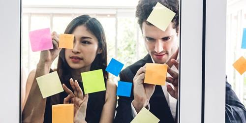 A woman and a man placing postit's on a glass pane.