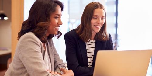 Photo of two women sitting in front of a laptop.