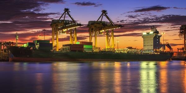 Container Cargo freight ship with working crane bridge in shipyard at dusk